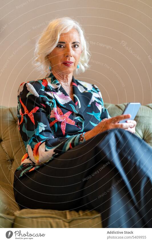 Ältere Frau sitzt auf dem Sofa und benutzt ihr Smartphone Textnachricht benutzend Kommunizieren Komfort Internet online zu Hause Senior älter gemütlich