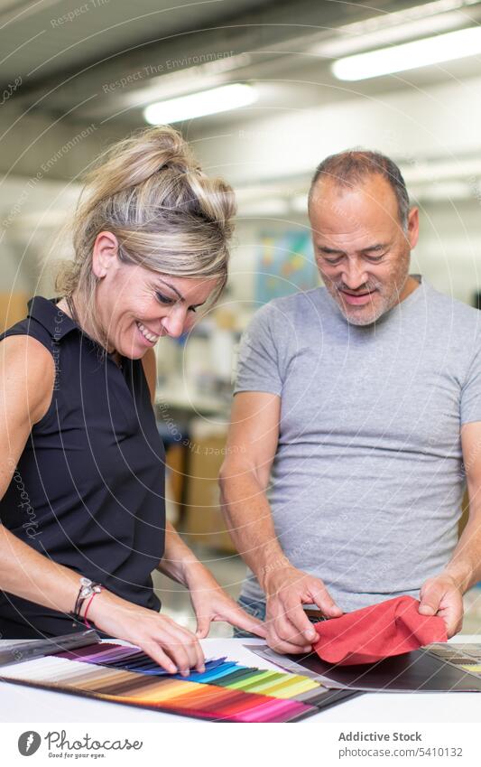 Glücklicher Mann mittleren Alters und erwachsene Frau, die bunte Stoffmuster im Tageslicht untersuchen Probe Lächeln Herstellung Fabrik Qualität Textil prüfen