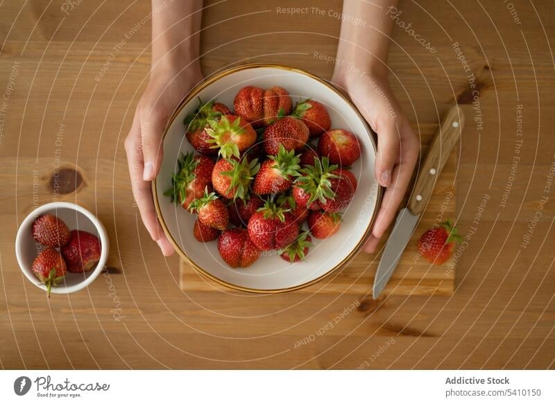 Crop-Frau hält Erdbeere in Schale über Holztisch Person Erdbeeren reif Lebensmittel frisch Marmelade süß vorbereiten Frucht geschmackvoll lecker Vitamin