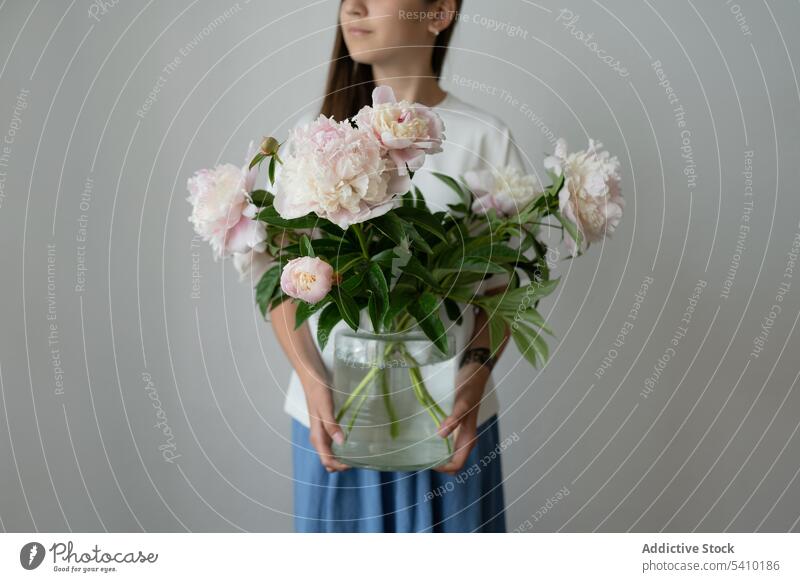 Unerkanntes Kind im Vorschulalter mit blühenden Pfingstrosen in einem Glasgefäß frisch Blütezeit Blume grün Blatt Vorbau einrichten geblümt Kleid Stil Vase