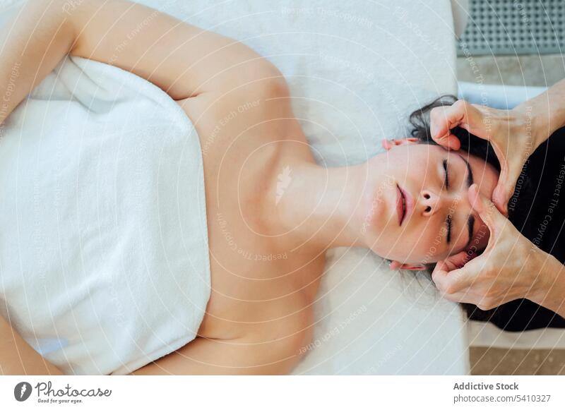 Junge Frau mit dem Rücken auf dem Bett liegend während einer Spa-Therapie Gesicht Massage Handtuch Hautpflege Masseurin Wellness Schönheit Lügen