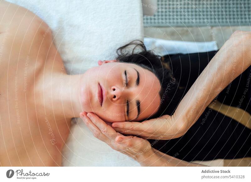 Junge Frau mit dem Rücken auf dem Bett liegend während einer Spa-Therapie Gesicht Massage Handtuch Hautpflege Masseurin Verfahren Wellness Schönheit Lügen