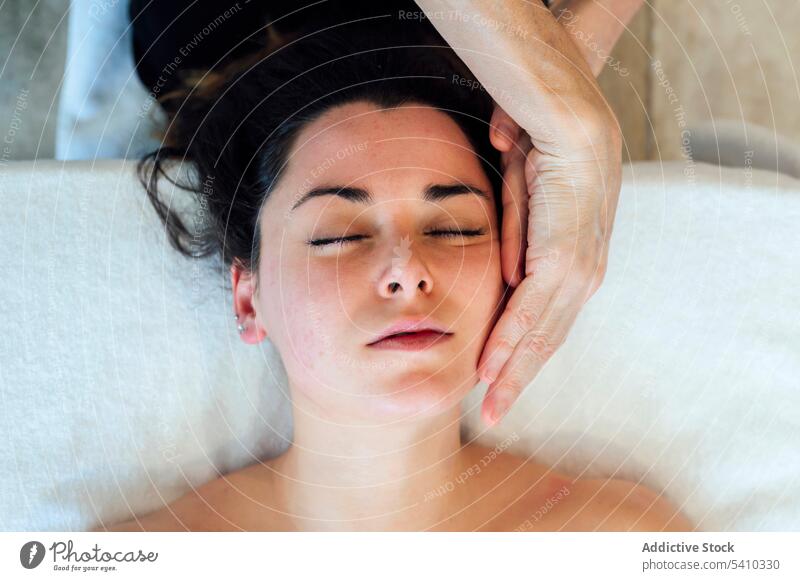 Junge Frau mit dem Rücken auf dem Bett liegend während einer Spa-Therapie Gesicht Massage Handtuch Hautpflege Masseurin Wellness Schönheit Lügen