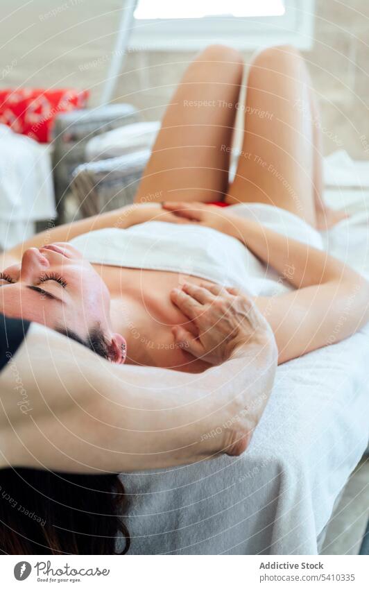 Junge Frau auf dem Bett liegend während einer Gesichtsmassagetherapie Spa Massage Handtuch Therapie Masseurin Schulter Verfahren Wellness Schönheit Lügen