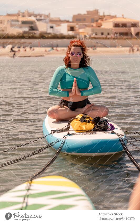 Glückliche Frau sitzt in einfachen Yoga-Pose auf Paddleboard im Meer Paddelbrett Schwimmer leichte Pose sitzen ruhen ernst MEER Erholung Wasser Sommer Resort