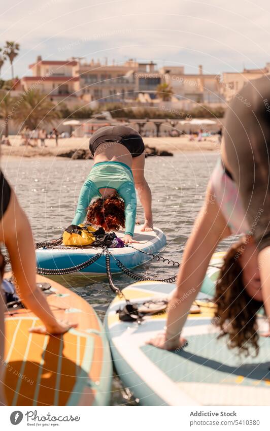 Junge Frauen in der Yogapose des nach unten gerichteten Hundes auf dem Paddelbrett nach unten gerichteter Hund Yogastellung üben Übung Hobby Wellness MEER Ufer