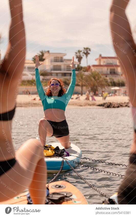 Frauen im Badeanzug bei Yoga-Übungen auf dem Paddelbrett Ausbilderin Strand Zusammensein üben Krieger-Pose Gleichgewicht Wellness Sommer Lächeln Badebekleidung