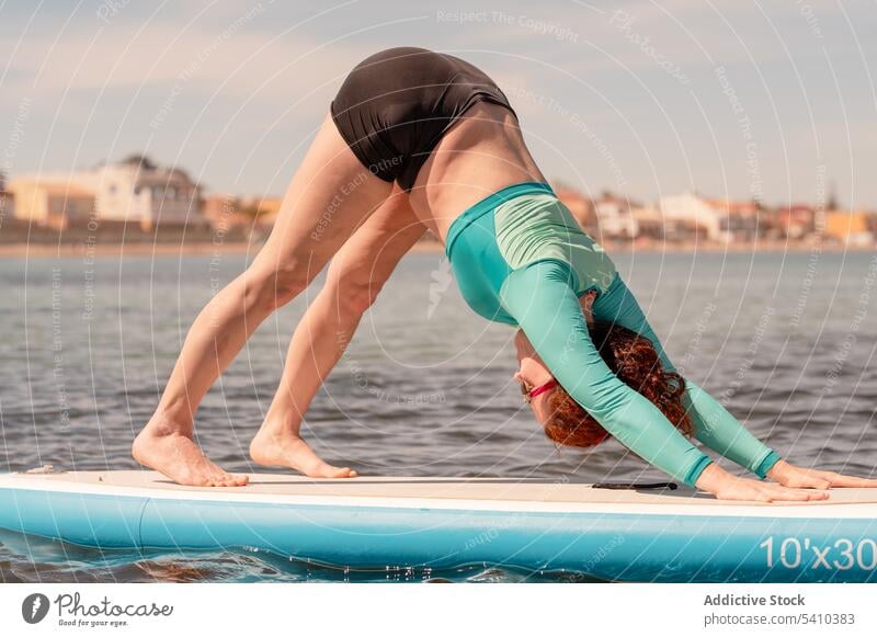 Frau macht Yoga auf Paddleboard über dem Meer Paddelbrett üben Dehnung nach unten gerichteter Hund Pose Strand Training MEER Meeresufer Aktivität Ufer beweglich