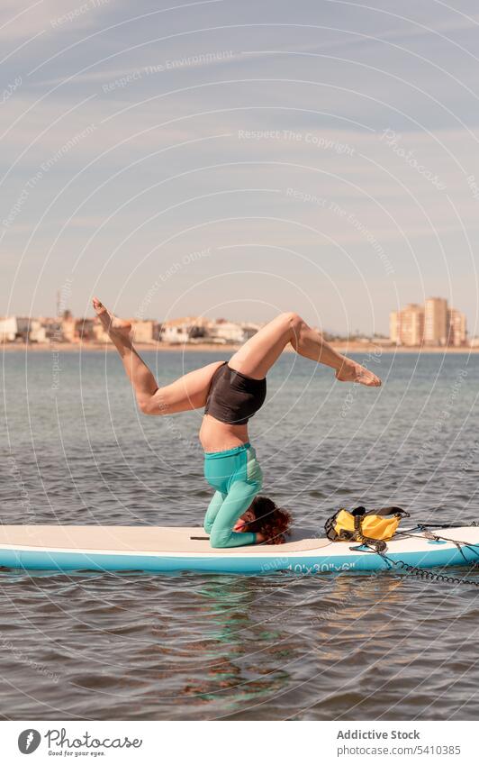 Frau macht Yoga mit Kopfstand und gespreizten Beinen auf dem Paddelbrett Pose Gleichgewicht üben beweglich Aktivität Sportbekleidung Wellness Salamba sirsasana
