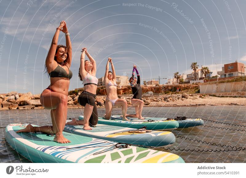 Gruppe von Frauen, die Yoga in der Haltung des Kriegers 1 machen Strand Dehnung üben Gleichgewicht Krieger-Pose Übung Aktivität Küste knien positionieren