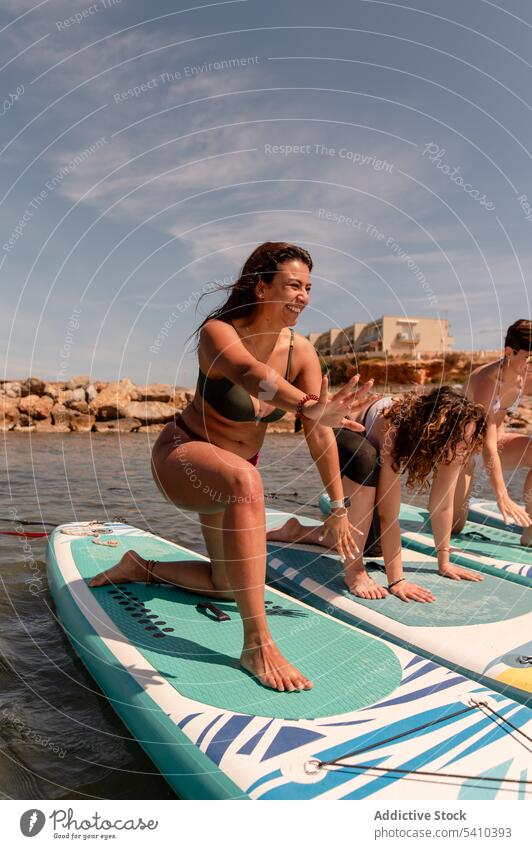 Junge Frauen machen Yoga-Übungen auf dem Paddleboard auf dem Meer üben Fitness MEER Gleichgewicht Paddelbrett Wohlbefinden virabhadrasana Sommer Glück