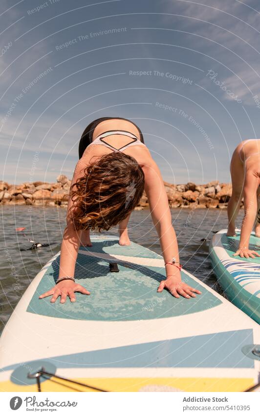 Anonyme Frau beim Yoga auf dem Paddelbrett über dem Meer üben Dehnung nach unten gerichteter Hund Pose Strand Training MEER Meeresufer Aktivität Ufer beweglich
