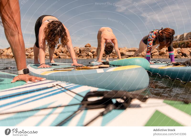 Frauen üben Yoga in vorwärts gefalteter Haltung auf dem Paddelbrett Übung Vorwärtsfaltung hohe Diele Pose Fitness Schiffsplanken MEER Wohlbefinden Sommer