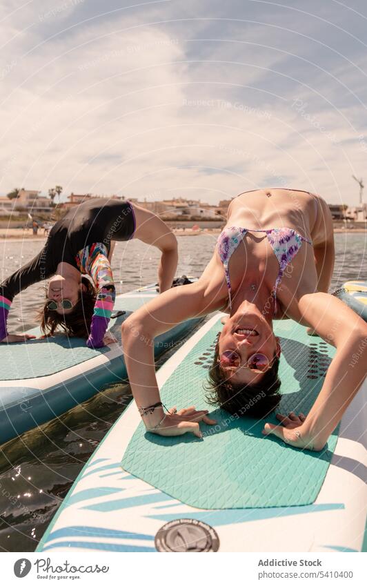 Frauen machen Yoga auf dem Paddelbrett bei Tageslicht Freundin üben Halbrad beweglich Gleichgewicht Badebekleidung Meerwasser jung wolkig Blauer Himmel Sommer