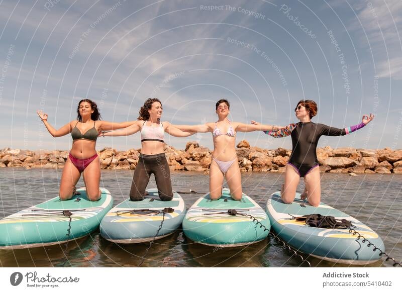 Gruppe junger Frauen in Bikinis kniend auf Paddleboards im Tageslicht Menschengruppe Lächeln Zusammensein Händchenhalten Badebekleidung Yoga positiv Paddelbrett