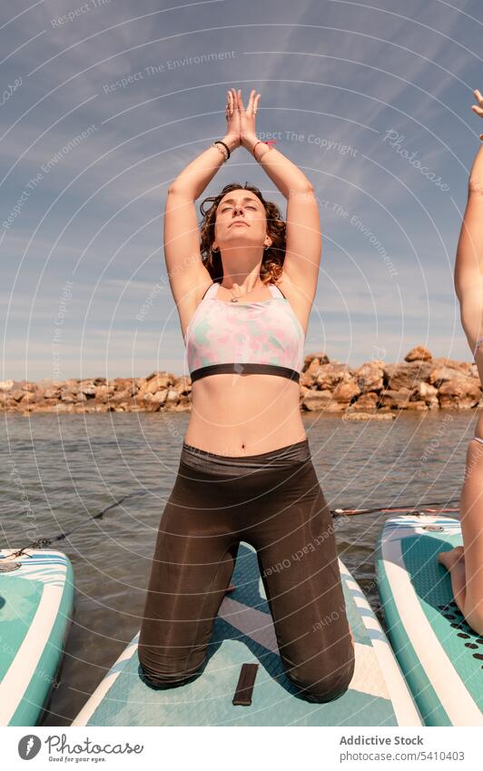 Junge Frau in Yoga-Pose auf dem Paddelbrett Freund Augen geschlossen Mudra Dehnung knien Berg mit erhobenen Armen jung Sommer wolkig Blauer Himmel tagsüber