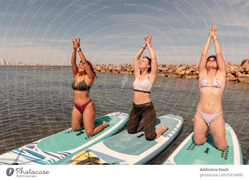 Gruppe junger Frauen in Yoga-Pose auf Paddelbrettern Menschengruppe Berg mit erhobenen Armen Augen geschlossen Mudra Dehnung knien Freund Sommer wolkig