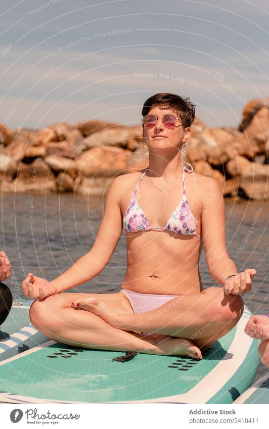 Schlanke Frau im Bikini meditiert auf einem Paddleboard im Meer Sup-Yoga Paddelbrett gyan mudra Zusatzplatine meditieren Gleichgewicht Zen Seeküste Mudra üben