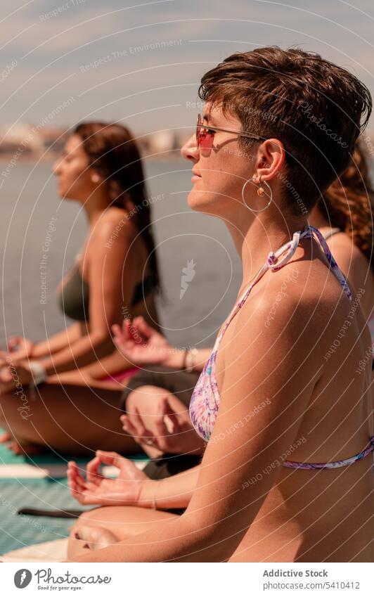 Junge Frauen sitzen in Padmasana-Pose auf Paddelbrettern Yoga Lotos meditieren üben Windstille Mudra Badebekleidung Konzentration jung Sommer Erholung Zen
