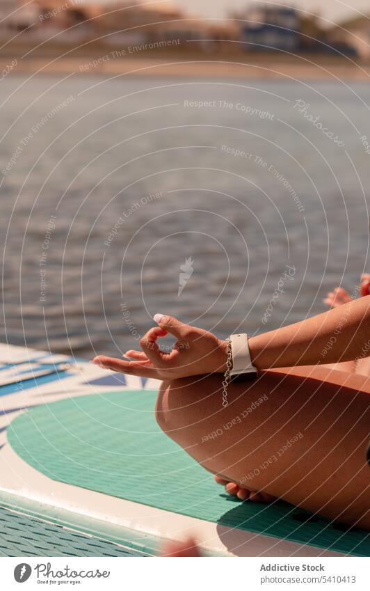 Crop Dame meditiert auf SUP-Board in ruhigen Meer Sup-Yoga Paddelbrett gyan mudra Zusatzplatine Frau meditieren Gleichgewicht Mudra Seeküste Zen üben Windstille