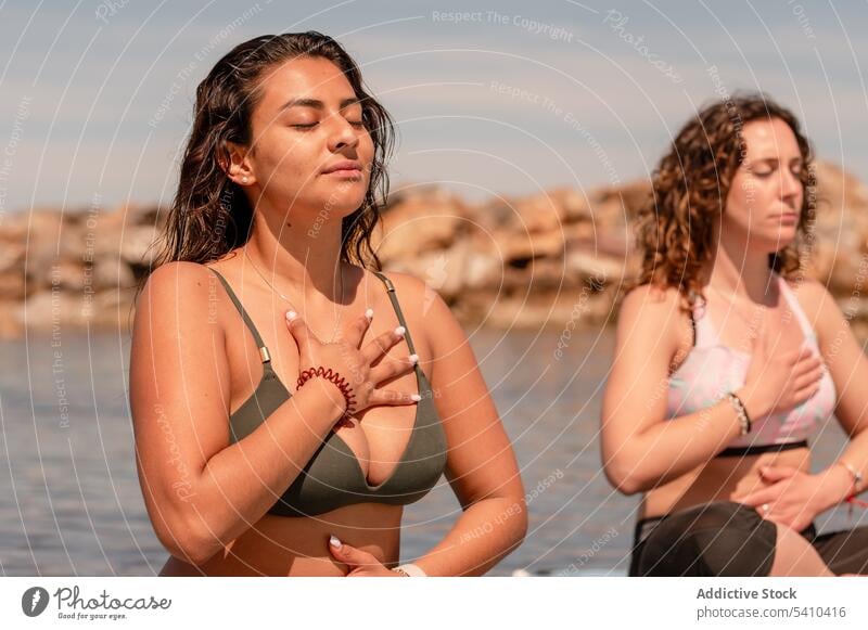 Frauen praktizieren Meditation beim SUP-Yoga am Meer Sup-Yoga Paddelbrett Zusatzplatine meditieren Gleichgewicht Zen Atem Seeküste üben Windstille Harmonie Pose