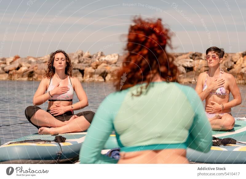 Frauen praktizieren Meditation beim SUP-Yoga am Meer Sup-Yoga Paddelbrett Zusatzplatine meditieren Gleichgewicht Zen Atem Seeküste üben Windstille Harmonie Dame