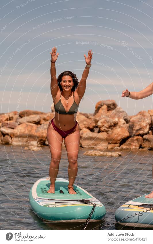 Fröhliche Frau mit erhobenen Armen Krieger 1 Yoga-Pose auf Paddleboard Übung üben Fitness MEER Gleichgewicht Krieger-Pose Schutzschild Glück Wohlbefinden