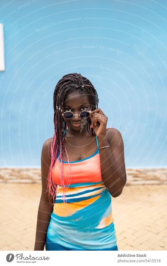 Schwarze Frau mit Sonnenbrille an blauer Wand Sommer Outfit trendy Stil Straße stehen selbstbewusst jung Brille Zopf Porträt sinnlich Afro-Look elegant