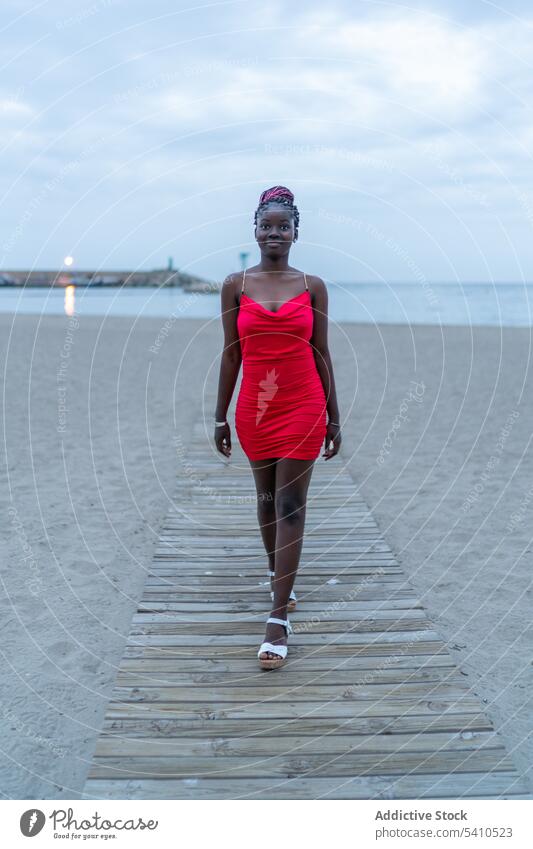 Glückliche afroamerikanische Frau, die auf einem Pier spazieren geht Spaziergang Meer Stil MEER selbstbewusst Himmel ernst Kleid Mode trendy Dame Natur rot