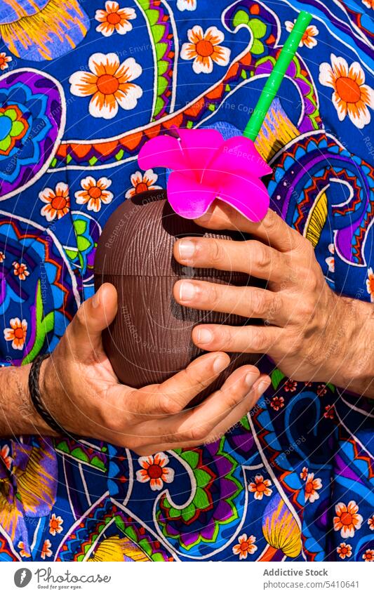 Männlicher Crop im bunten Hemd hält Kokosnuss-Cocktail Frucht Getränk Resort Armband Erfrischung tropisch Stroh trinken exotisch Mann hawaiianisch Bekleidung