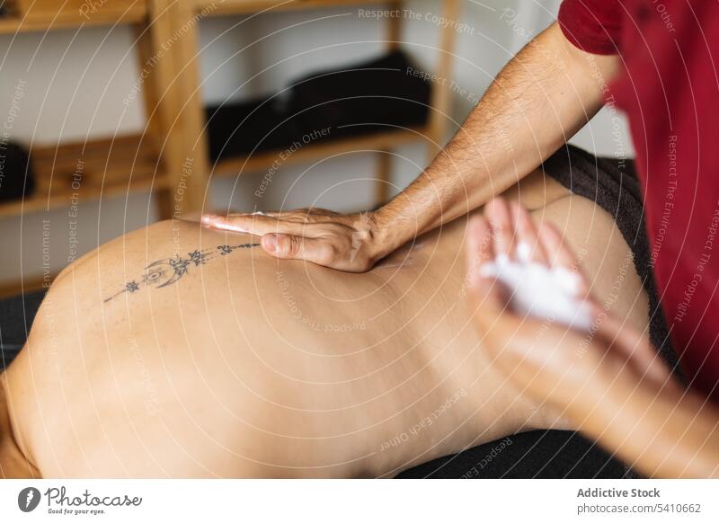 Unbekannter Masseur cremt anonyme Frau mit tätowiertem Rücken am Tag ein Klient Massage Tattoo bewerben Sahne Tisch Salon männlich professionell Spezialist
