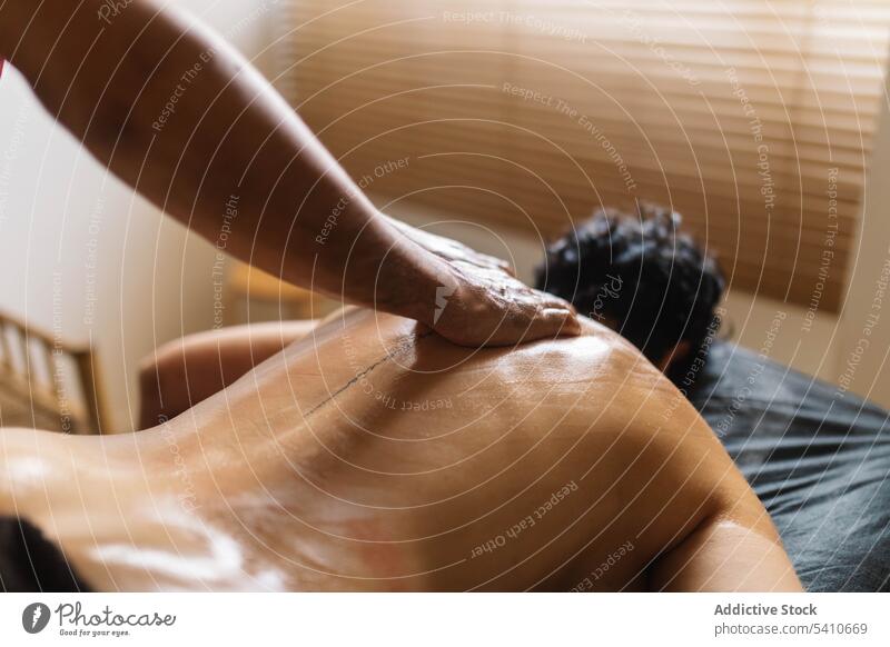 Unbekannter Masseur trägt Öl auf den tätowierten Rücken einer anonymen Frau bei Tag auf Klient Massage bewerben drücken Tisch Spezialist Salon männlich