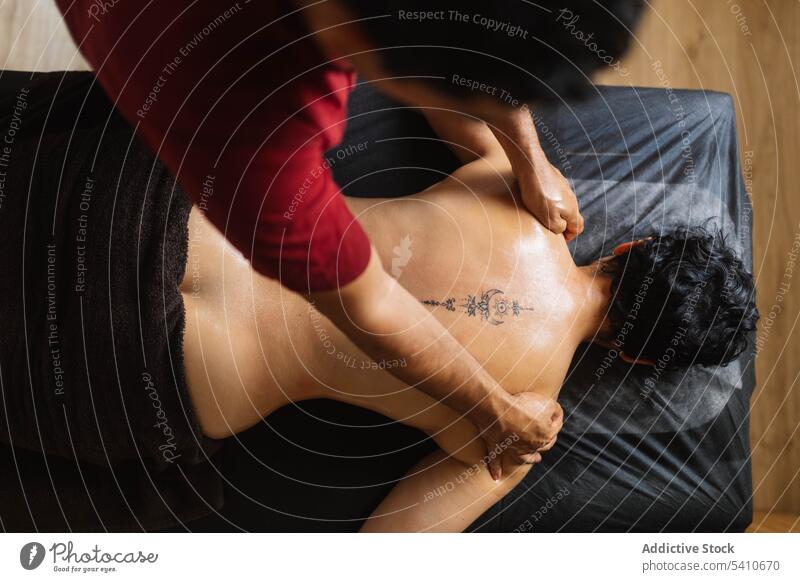 Unbekannter Masseur trägt ayurvedisches Öl auf den tätowierten Rücken einer anonymen Frau auf Klient Massage bewerben drücken Schulter Tisch Spezialist Salon