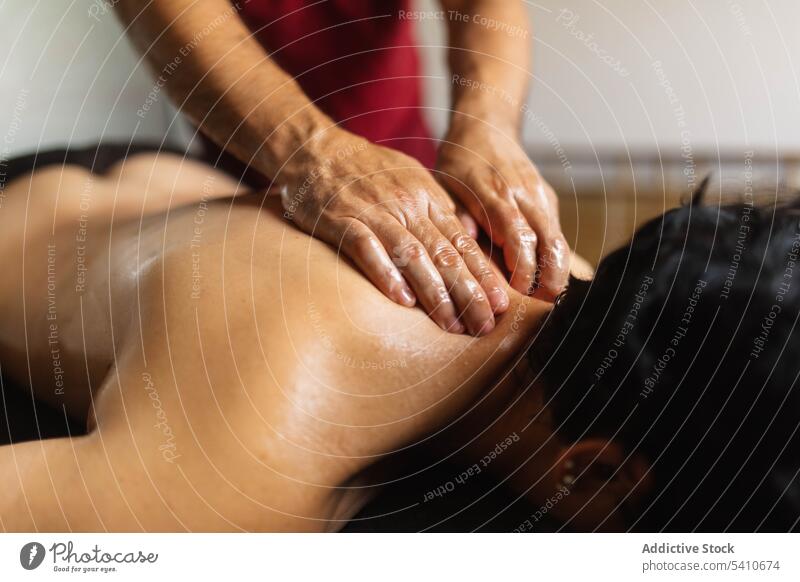 Masseur bei der Anwendung von ayurvedischem Öl auf dem Rücken einer anonymen Frau am Tag Klient Massage bewerben drücken Schulter Tisch Spezialist Salon