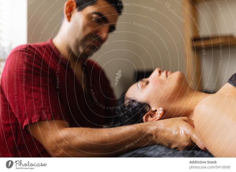Ethnischer erwachsener Masseur behandelt eine auf dem Bett liegende Frau mit therapeutischer Massage umhüllen Handtuch Verfahren Leckerbissen Schulter Muskel