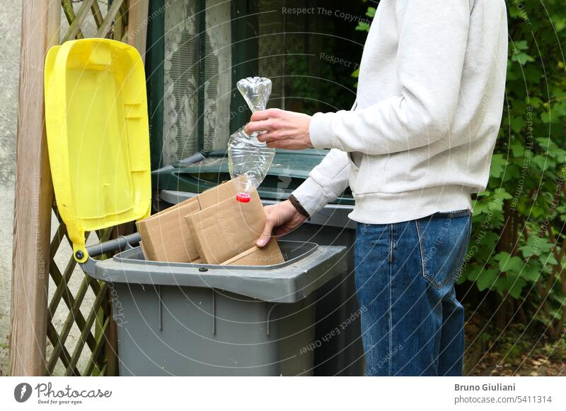 Ein Mann sortiert Abfall. Eine Person wirft Kartonverpackungen und eine Plastikflasche in eine gelbe Recyclingtonne. Behälter Flasche Ökologie umgebungsbedingt