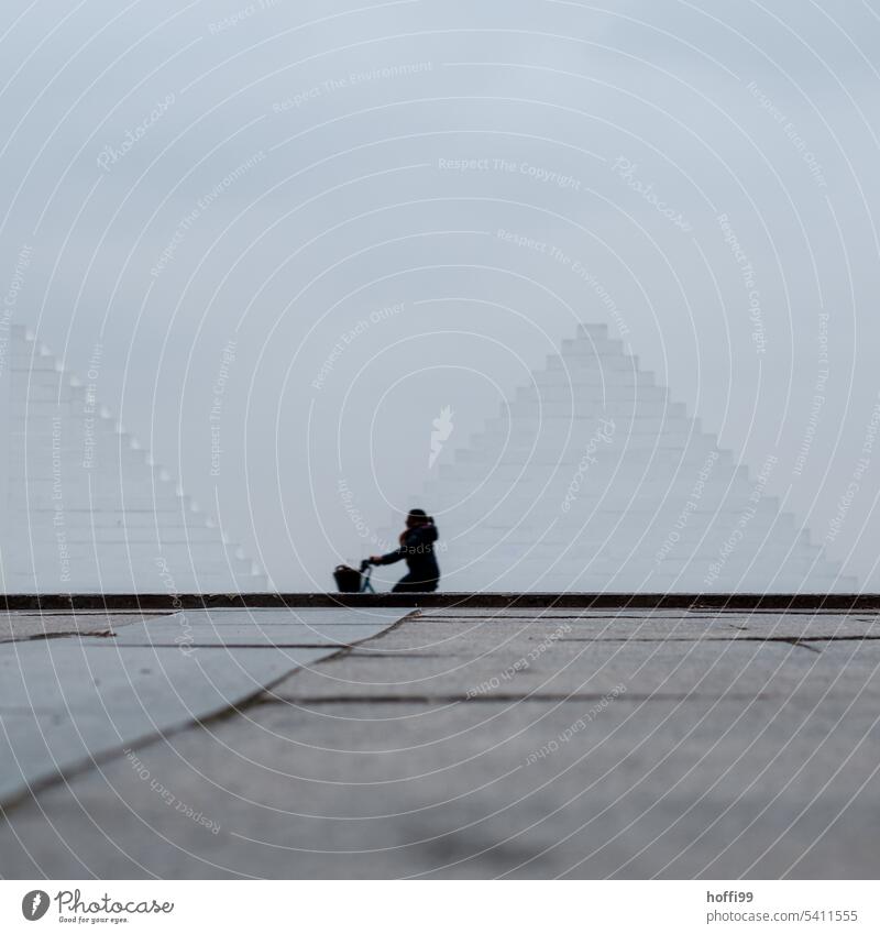 Silhouette eines Menschen auf einem Fahrrad vor weißer, pyramidenförmigen Mauer Nebel Dunst Wege & Pfade Ziel Einsamkeit minimalistisch urban Tristesse