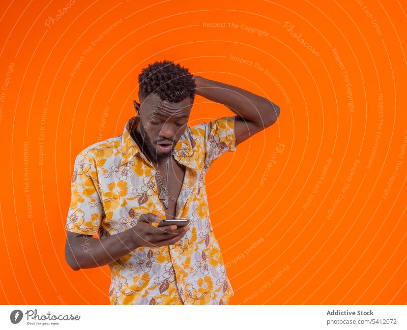 Überraschender junger Afroamerikaner in Freizeitkleidung, der auf den Bildschirm seines Mobiltelefons schaut Mann Smartphone benutzend Textnachricht Surfen