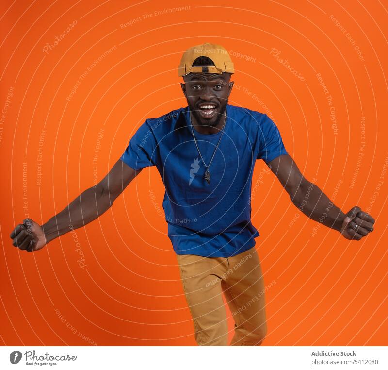Fröhlicher Afroamerikaner mit runder Mütze tanzt Mann Lächeln Tanzen Stil Glück heiter gestikulieren lässig froh Optimist Spaß aufgeregt Hip-Hop Mode aktiv