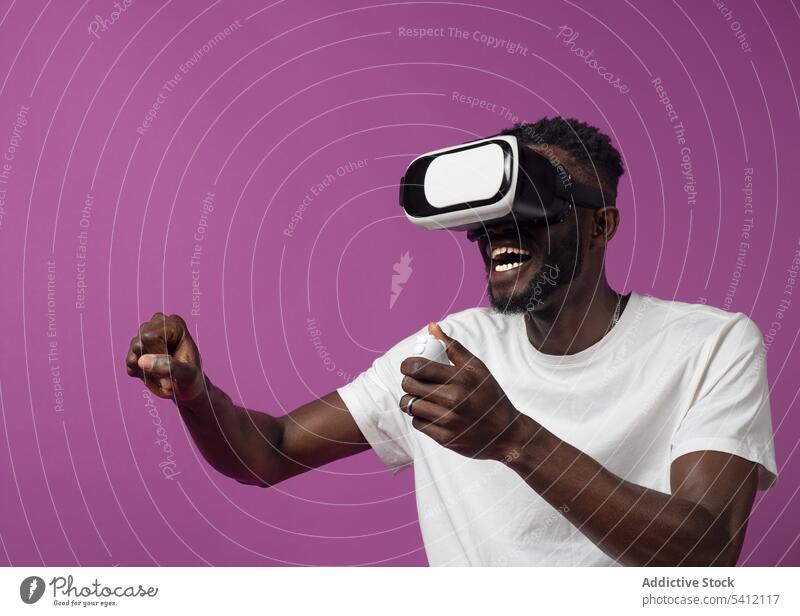 Fröhlicher junger schwarzer Mann, der ein Video über ein Virtual-Reality-Headset betrachtet aufgeregt Regler Virtuelle Realität Videospiel Schutzbrille