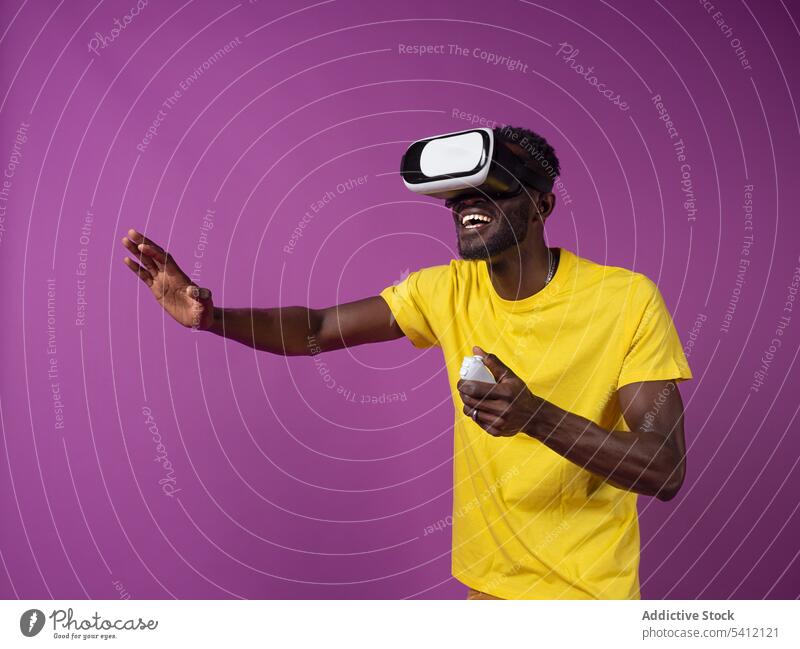 Fröhlicher junger schwarzer Mann sieht sich einen Film auf einem Virtual-Reality-Headset an aufgeregt Regler Virtuelle Realität Videospiel Schutzbrille