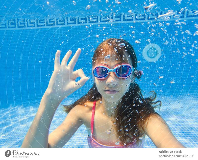 Positives Mädchen mit Brille gestikuliert OK im Schwimmbad schwimmen Wasser Pool Finger Zeichen gestikulieren Badebekleidung Porträt selbstbewusst Urlaub