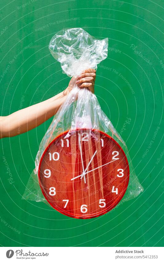 Crop Person hält Plastiktüte mit roter Uhr im Studio Hand Kunststoff Tasche Zeit Halt Konzept zeigen durchsichtig Wand grün rund Paket Minute manifestieren