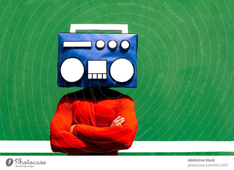 Anonyme Person, die ihr Gesicht mit einer blauen Boombox bedeckt Mann zuhören Musik Radio Deckblatt die Arme verschränkt rot Tierhaut cool hell Individualität