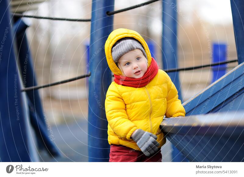 Niedlicher kleiner Junge hat Spaß auf einem Spielplatz im Freien hölzern Aufstieg Kind Schiff spielen Winter Tag kalt Spielzeit Gerät lässig Kindergarten