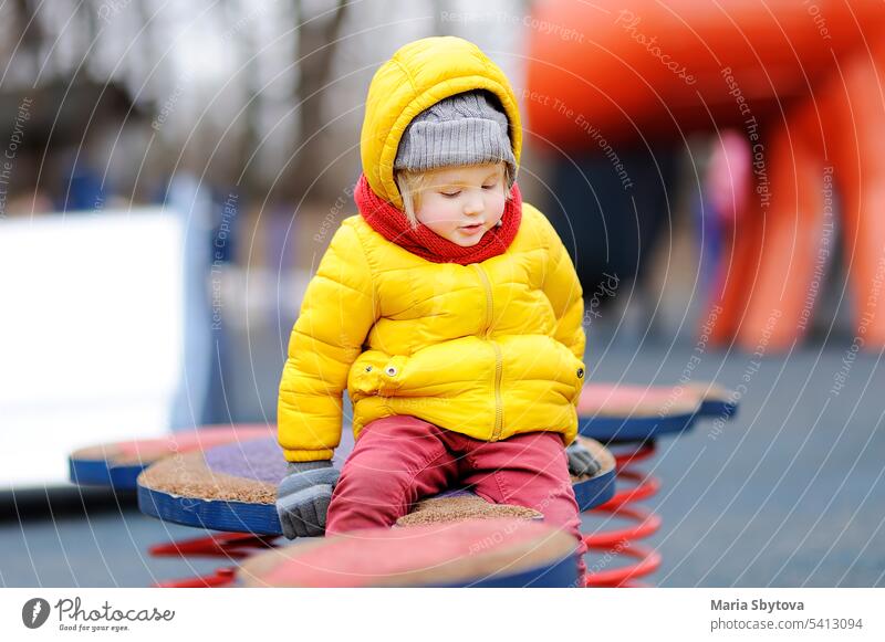 Niedlicher kleiner Junge hat Spaß auf einem Spielplatz im Freien Winter kalt Kind Kleinkind Tag hölzern Gerät spielen teeter Wippe eiern Spielzeit lässig