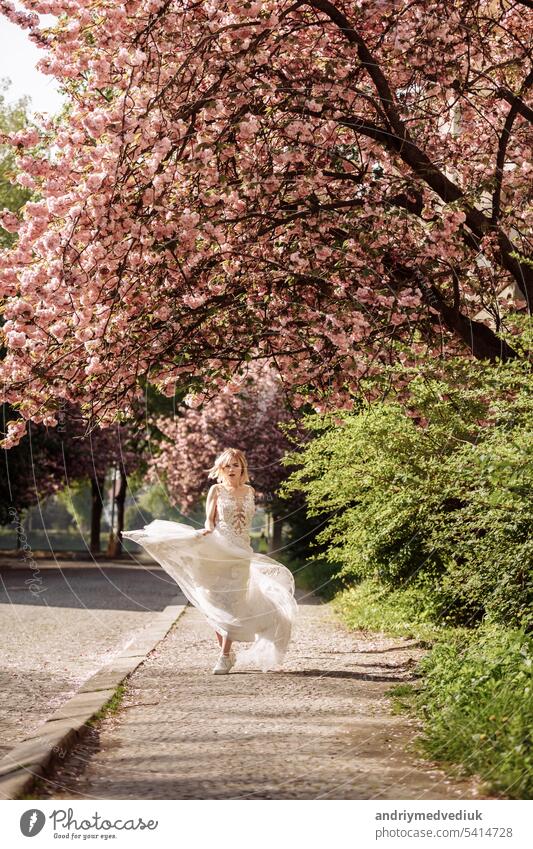 Frauentag. schöne junge Frau in luxuriösen langen Kleid in der Nähe von blühenden Sakura. stilvolle Mädchen in der Nähe von blühenden Sakura Blumen auf dem Hintergrund in den Frühling Park. Harmonie mit der Natur Konzept
