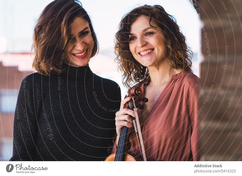 Junge lächelnde Frauen mit Geige auf Balkon Musiker jung Lächeln elegant Freund Instrument heiter Kunst Klang Spielen Leistung Melodie Geiger Klassik schön