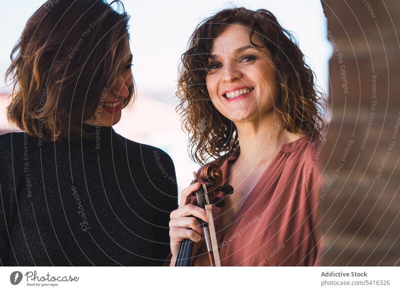 Junge lächelnde Frauen mit Geige auf Balkon Musiker jung Lächeln elegant Freund Instrument heiter Kunst Klang Spielen Leistung Melodie Geiger Klassik schön