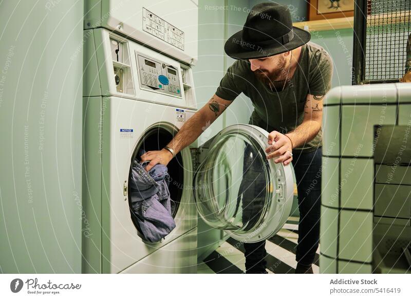 Gut aussehender Mann, der Wäsche in die Waschmaschine faltet gutaussehend bärtig Falten Erwachsener Model Wäscherei jung selbstbewusst männlich lässig Blick